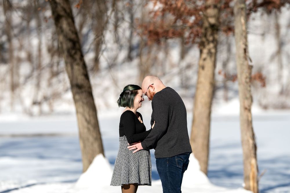 Pregnant couple sharing a tender forehead kiss surrounded by snow-covered trees in a winter park.