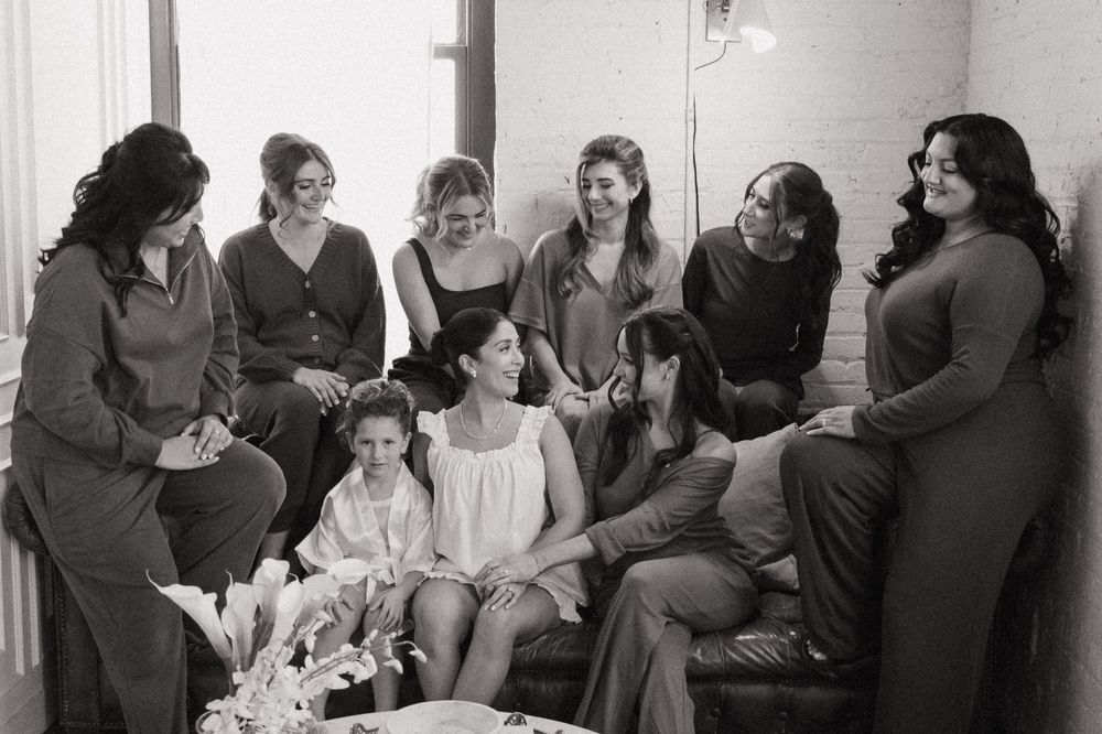 Wedding party members sit and chat in a bright white room with natural lighting.