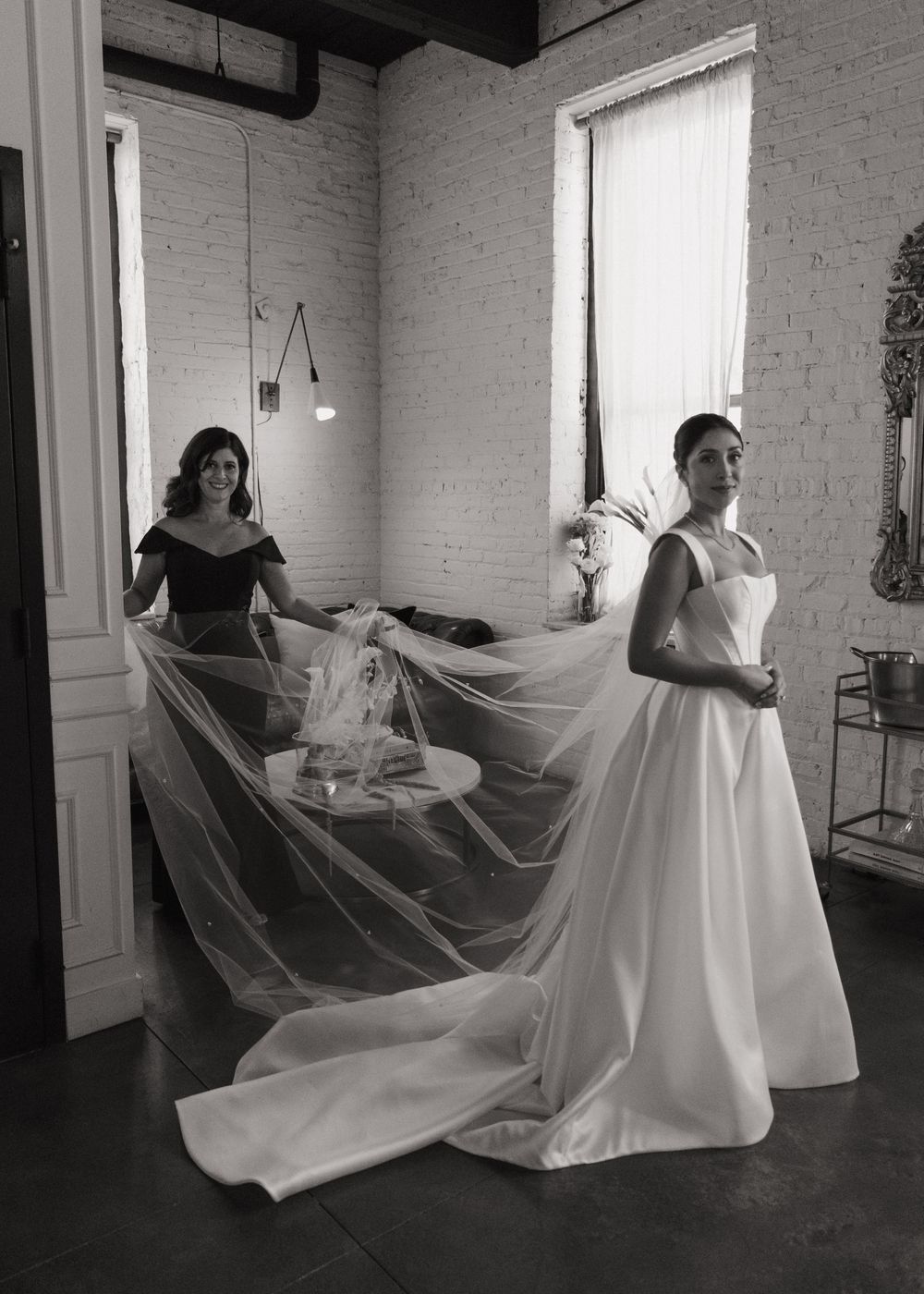 A flowing white wedding dress twirls gracefully in a bright studio space with brick walls and large windows.
