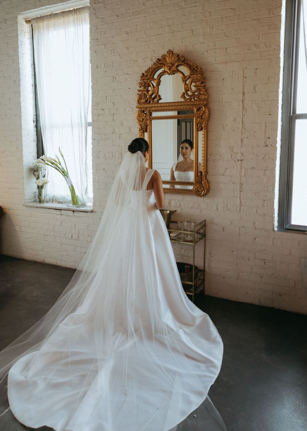 An elegant white wedding dress with a flowing train displayed in an industrial loft space with exposed brick walls.