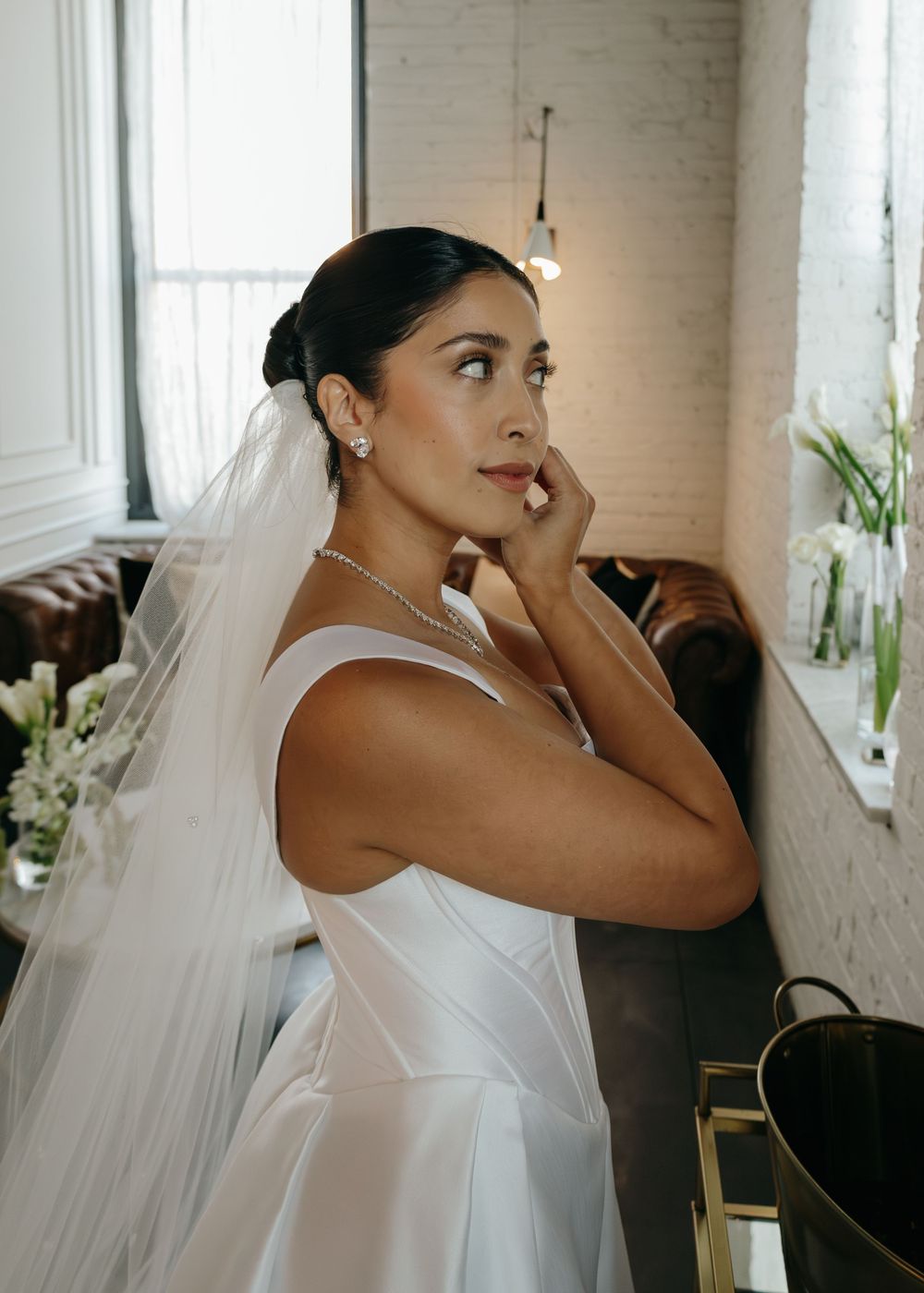 Bride in a sleek white wedding dress and veil shows emotional reaction during a candid moment at a venue.