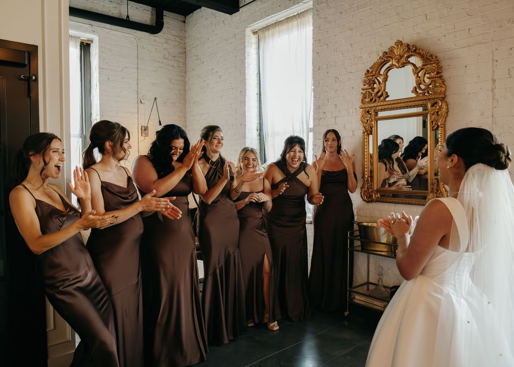 Bridesmaids in matching brown dresses gather around a bride in white during a wedding preparation moment.