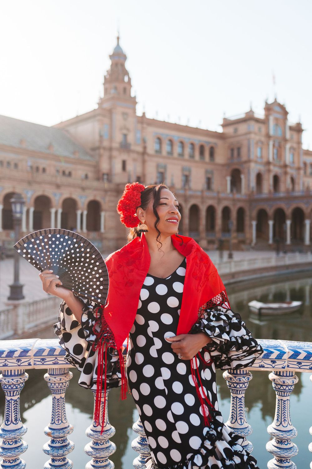 Flamenco dancer in polka dot dress with red shawl and fan poses at Plaza de España, Seville, Spain.