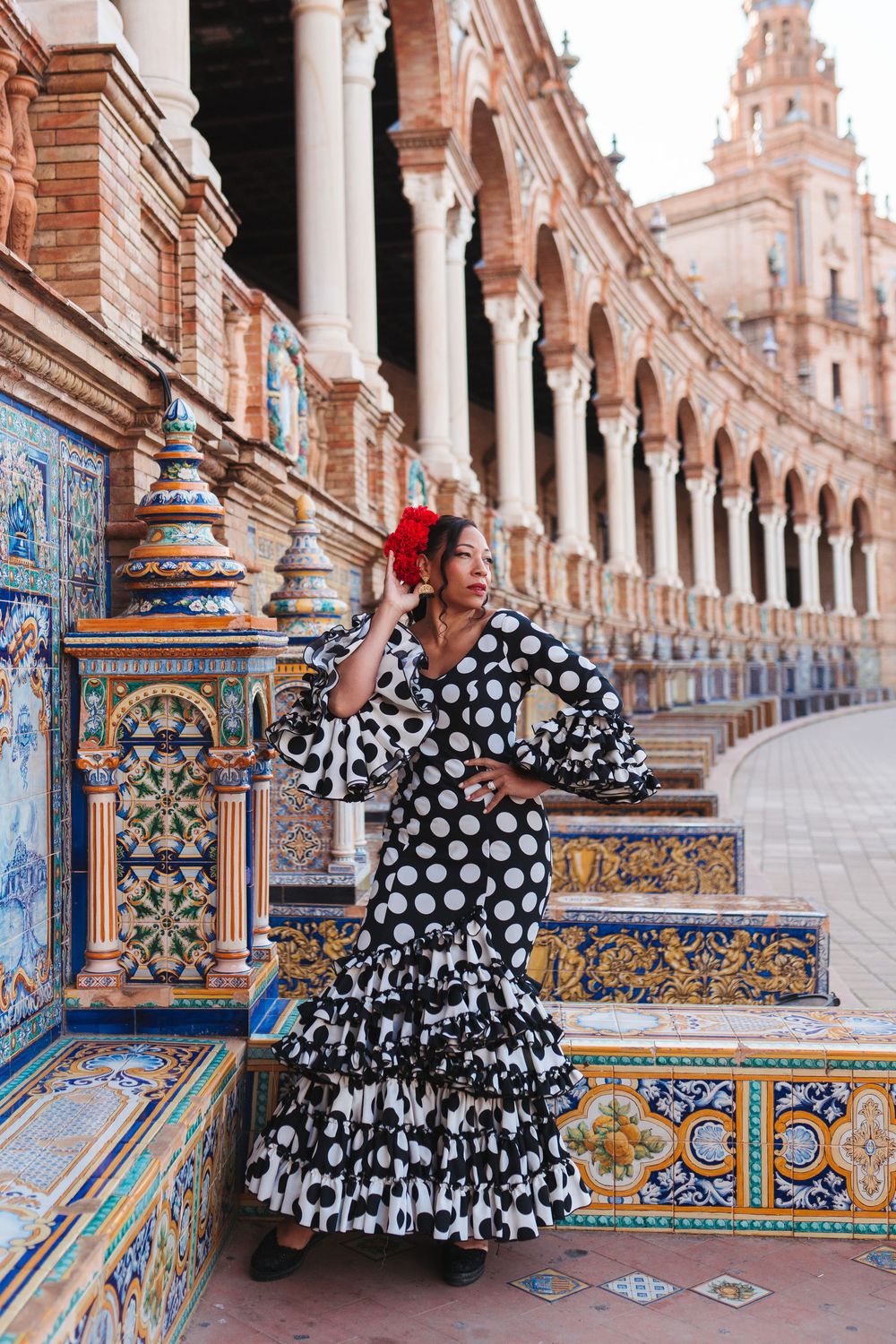 Flamenco dancer in black and white polka dot dress poses at Plaza de España Seville Spain.