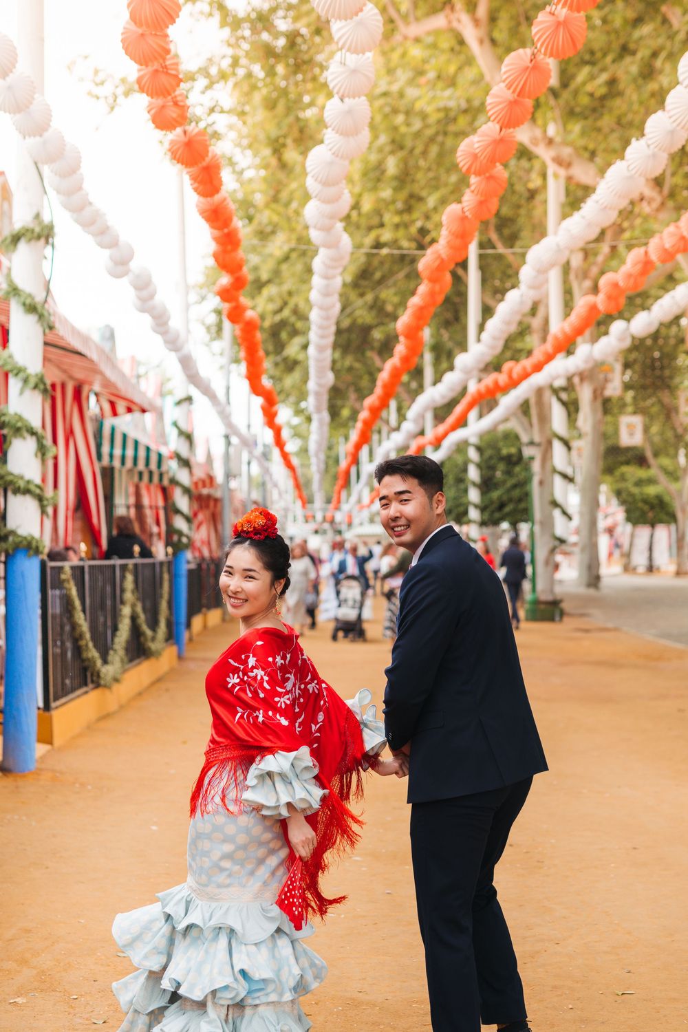 A couple in traditional dress celebrates under festive red and white paper lantern decorations at an outdoor festival.