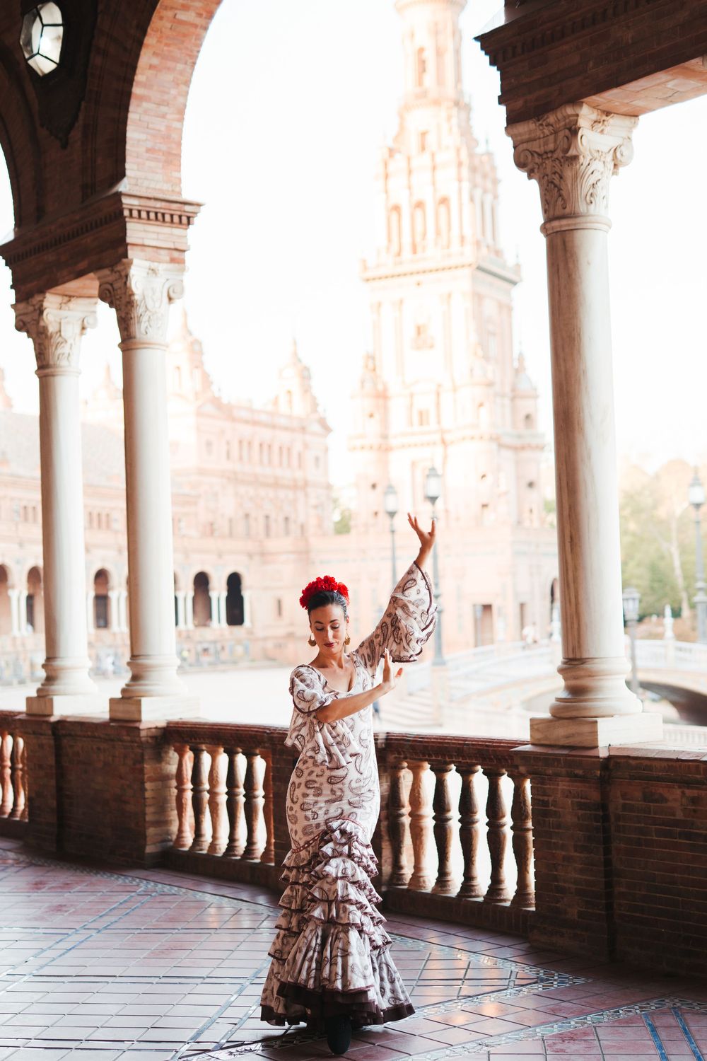 Woman in flamenco dress twirls gracefully under ornate archways at Plaza de Espana in Seville, Spain.