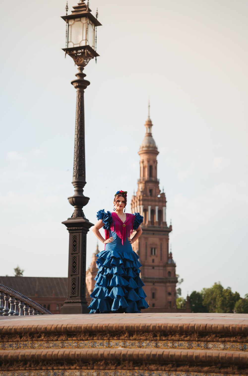 A sequence of photos showing a person in a vibrant blue flamenco dress posing on a stone wall at Plaza de España in Seville.