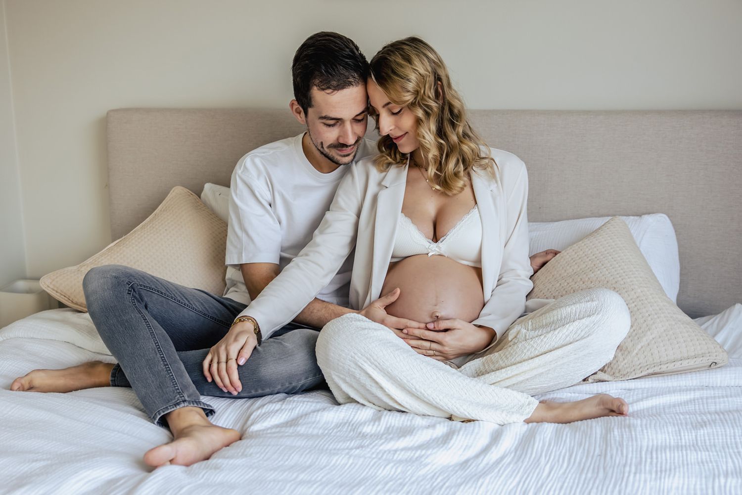 Warme kleurenfoto van een zwangerschapsshoot in de slaapkamer in Noord-Holland. Samen zittend op bed met een blote zwangere buik