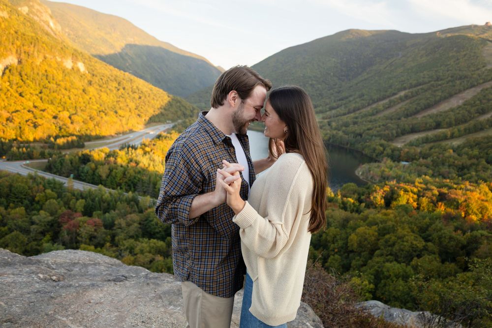 A couple shares a romantic moment at sunset in the mountains with golden light illuminating the landscape.