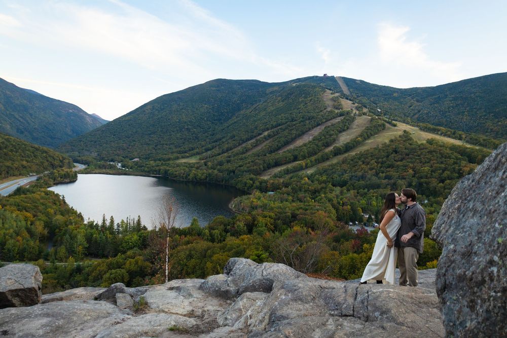 Panoramic mountain landscape view showing green peaks and a lake in the valley.
