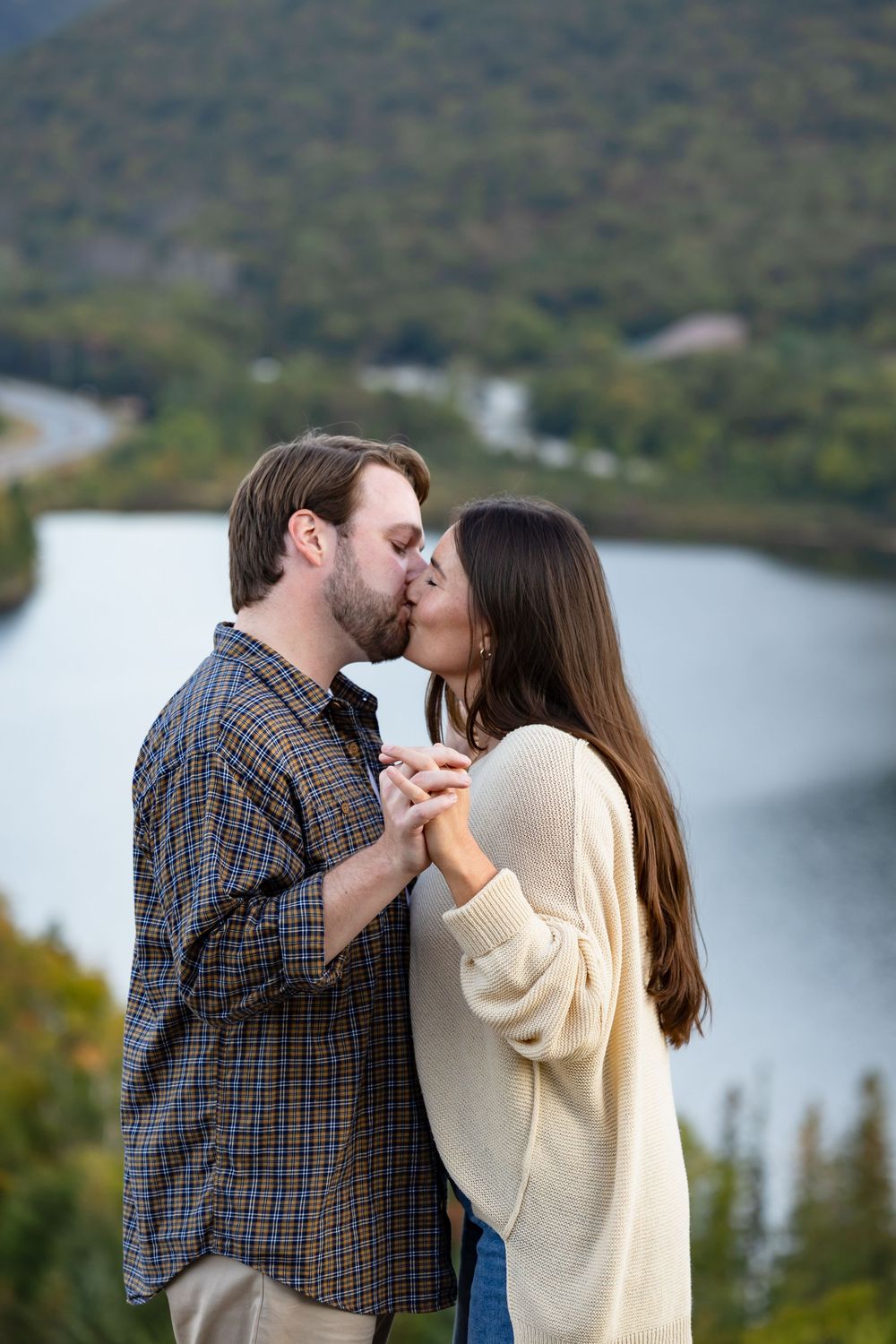 A couple shares a romantic kiss against a scenic mountain lake backdrop on an autumn afternoon.