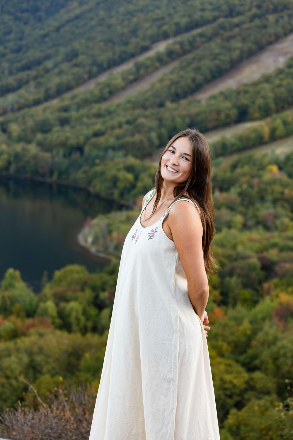A white dress twirls against a scenic mountain backdrop with a lake and autumn foliage in the distance.