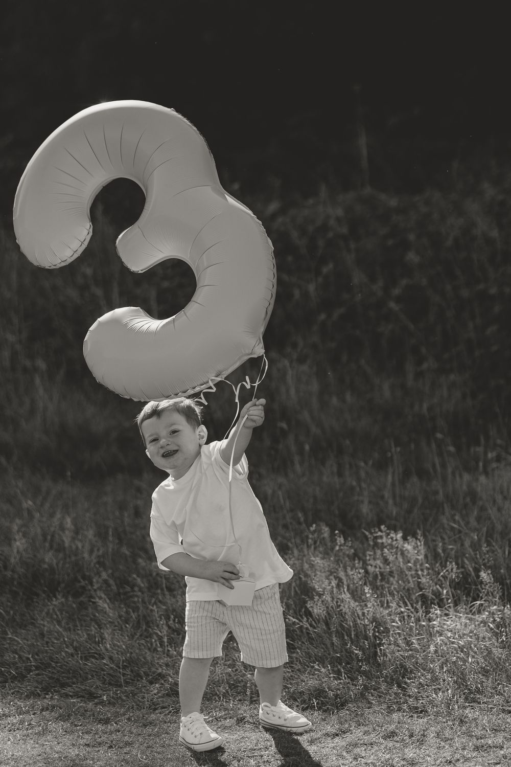 A black and white photo of a large number three balloon being carried proudly in a field.