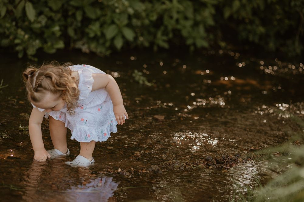 A white dress flutters as someone splashes in shallow water surrounded by greenery.