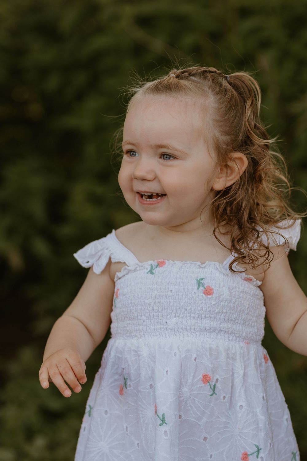 A delicate white smocked dress with pink floral details sparkles in natural light.