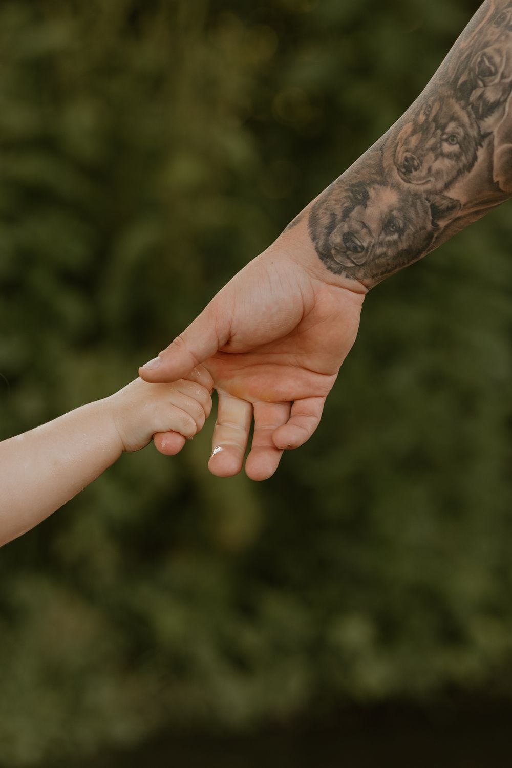 A daughter wraps her hands around her dad's finger against a green background.