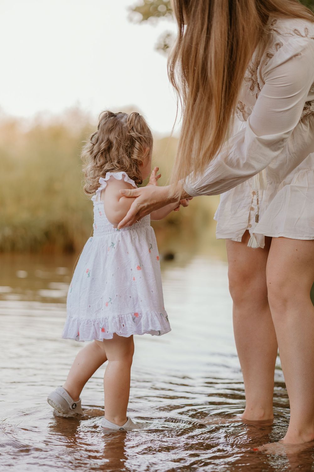 Mother and daughter frolicking in the shallow water wearing white dresses at sunset.