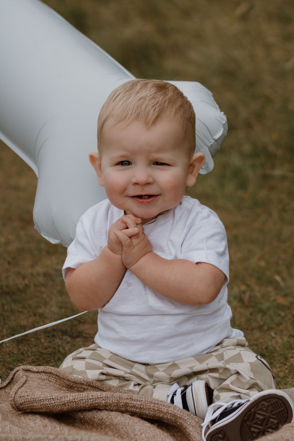 A baby in white shirt sits on a blanket with inflatable decorations outdoors.