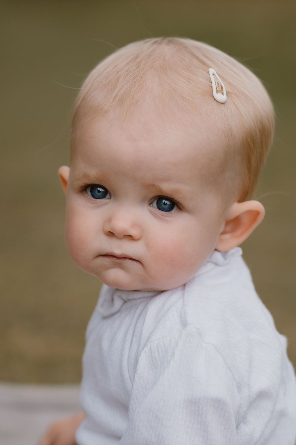 Close-up portrait of a baby in white clothing against a blurred natural background.