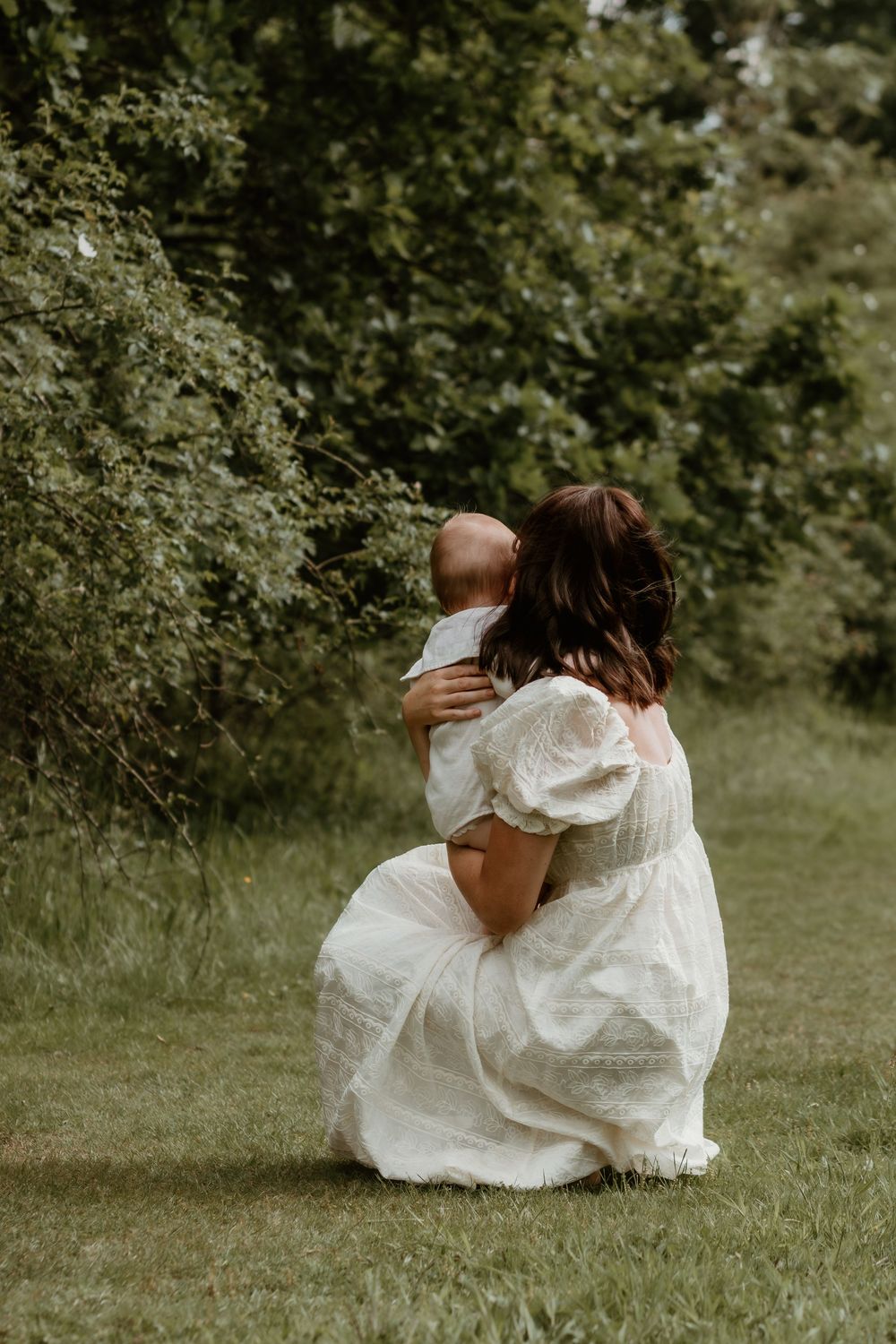 Artistic portrait of someone in a flowing white dress sitting in a grassy field.