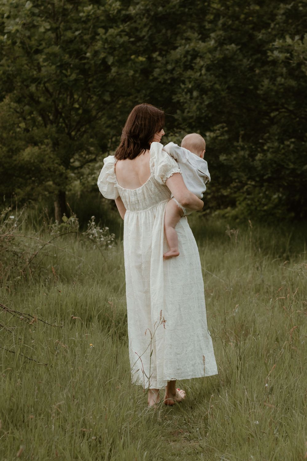 A mother walking barefoot in the son through a summer meadow.