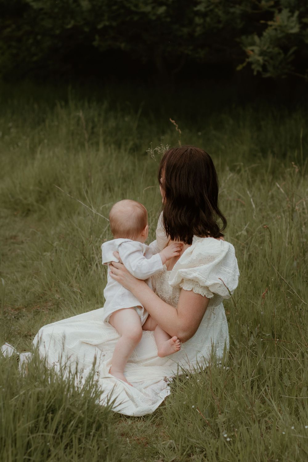 Intimate outdoor photography session for Mother and Baby featuring white dress details in tall grass.