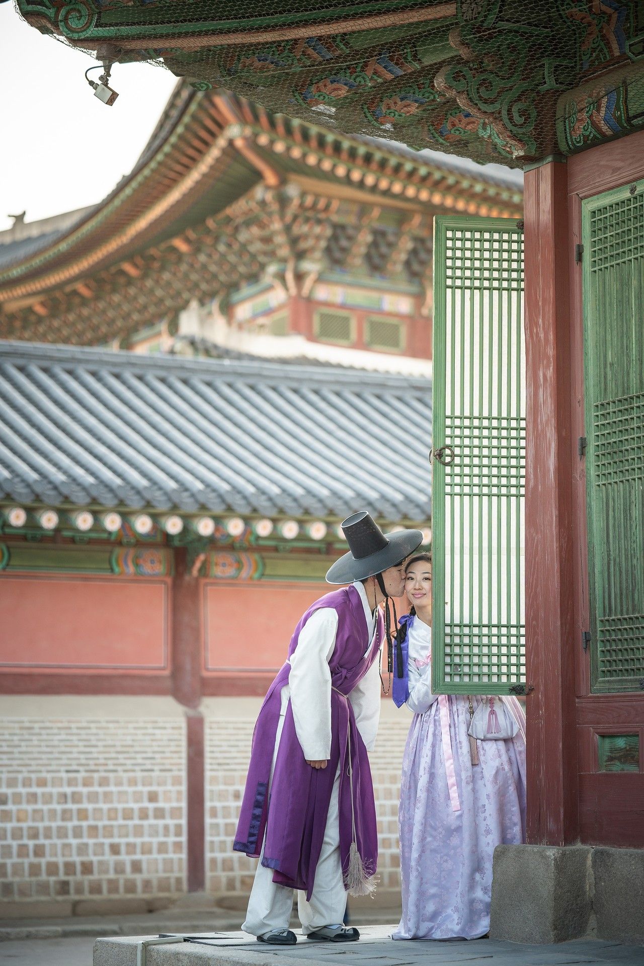 Traditional Korean palace officials in purple and white hanbok robes walk through ornate wooden corridors of historic architecture.
