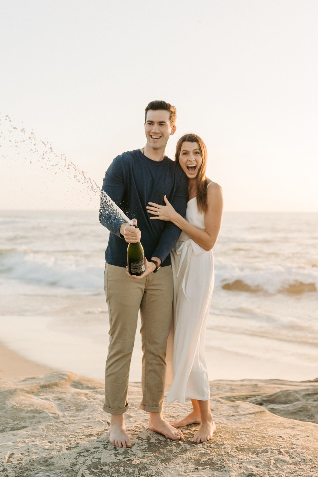 A couple celebrates with champagne on a sandy beach at sunset while sharing intimate moments together at Windansea Beach.