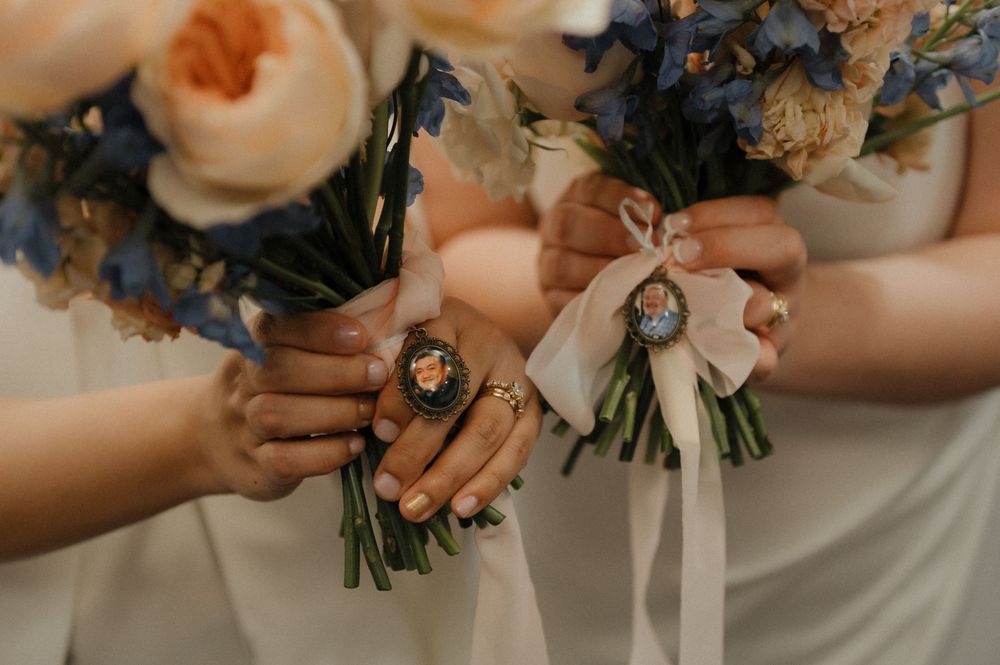 Close-up of wedding bouquets featuring peach roses and blue flowers tied with white ribbons.