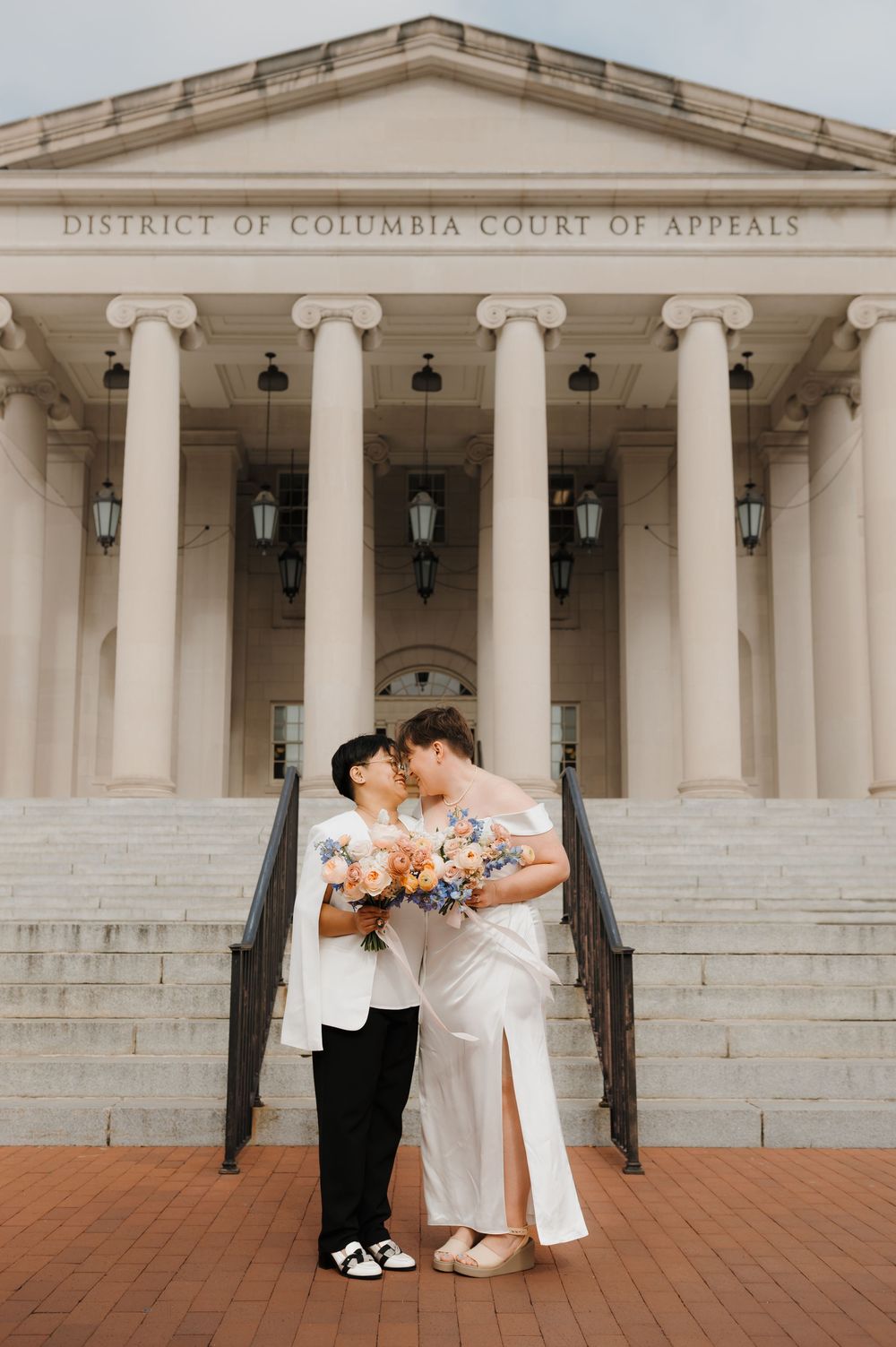 Wedding couple poses on steps of District of Columbia Court of Appeals building with white columns.