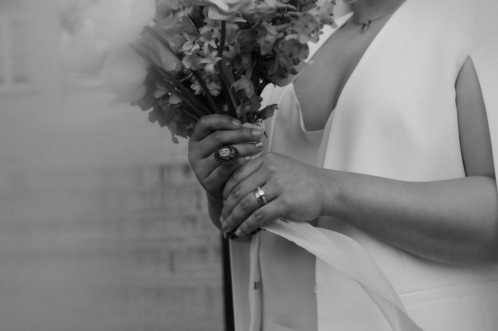 A romantic wedding photo showing a couple holding colorful floral bouquets against a neutral background.