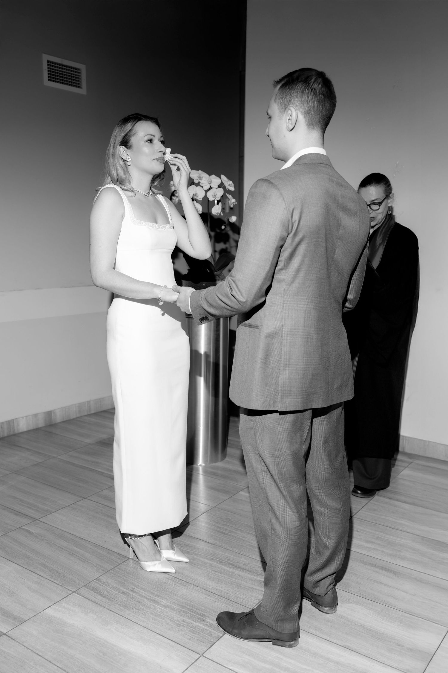 Wedding couple walks down the aisle at an indoor ceremony decorated with white chairs and dandelion-like light fixtures.