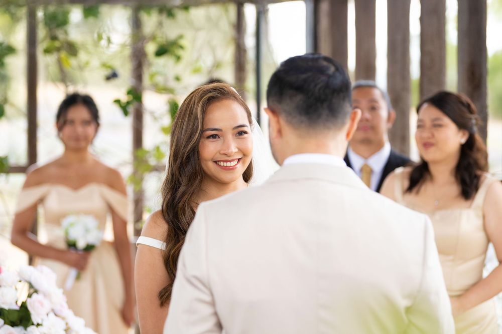 Bride smiling at groom during outdoor wedding ceremony with bridesmaids in background.