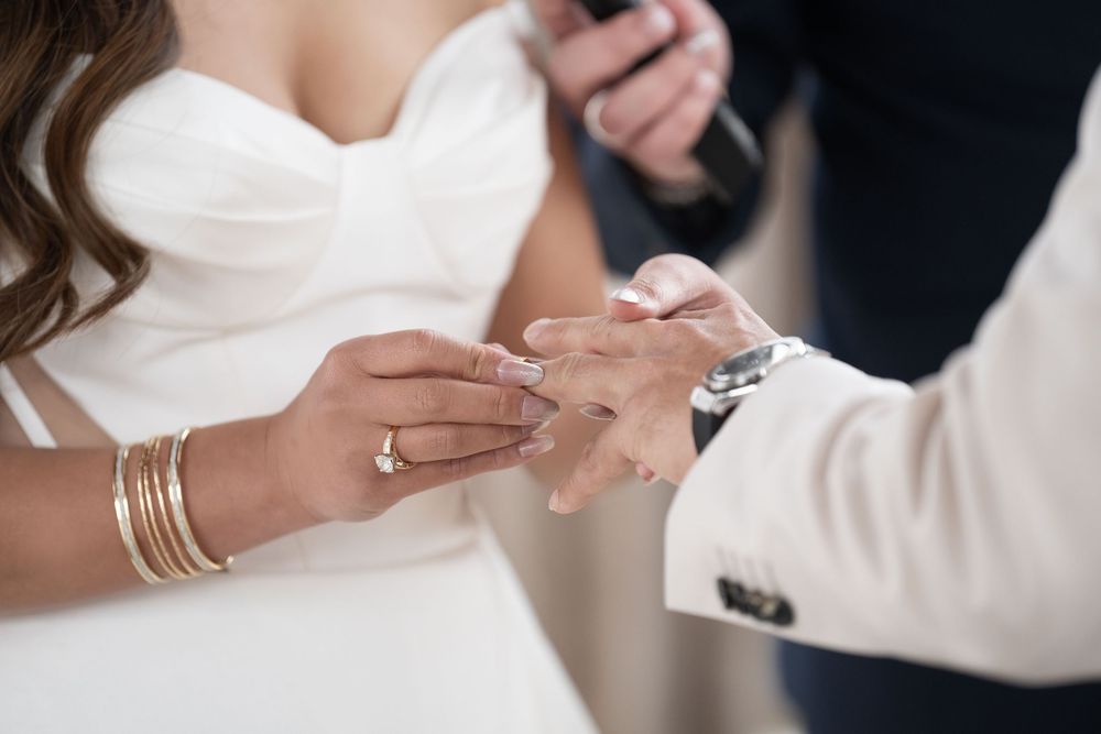 Close-up of groom placing wedding ring on brides finger during ceremony.