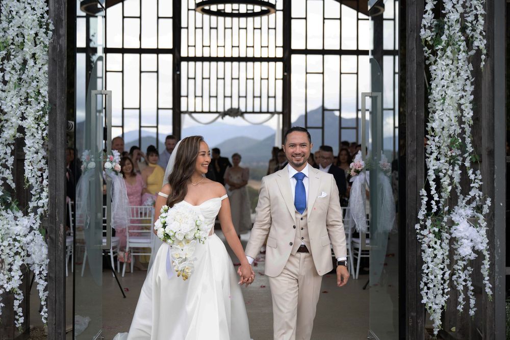 Newlyweds walking hand-in-hand through floral arch after wedding ceremony.