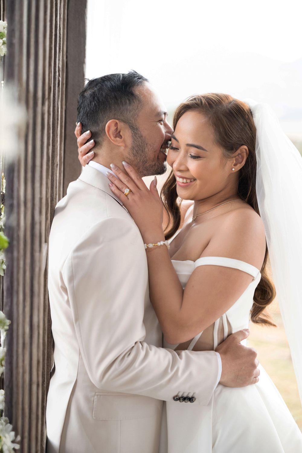Bride and groom share a tender embrace, with bride smiling as groom kisses her cheek.