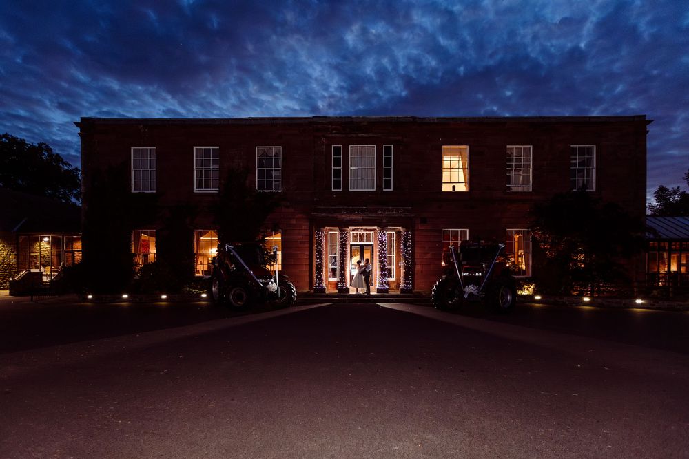 A historic brick mansion illuminated at night with warm glowing windows and dramatic evening sky.