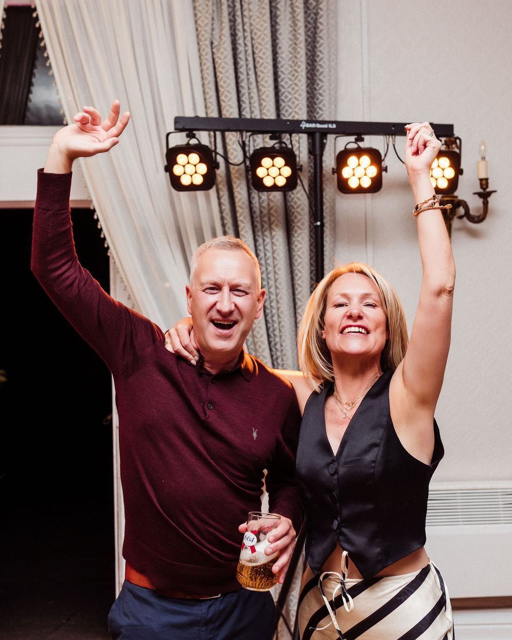 People dancing and having fun at a festive indoor celebration with white curtains in the background.