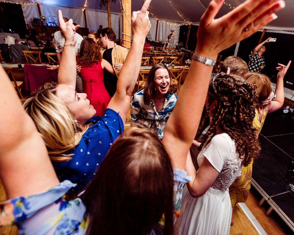 Energetic crowd with raised hands dancing and celebrating at a wedding reception.
