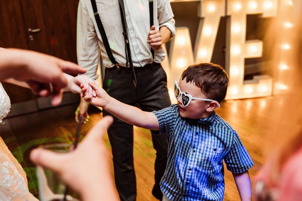 Wedding guests dance and celebrate on a lively dance floor illuminated by warm glowing lights.
