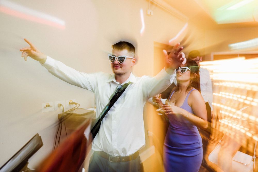 Wedding reception guests dancing and celebrating with raised arms in a dimly lit venue with string lights.