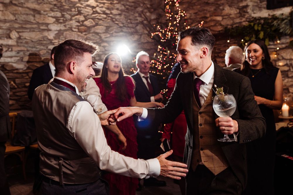 People dancing and celebrating at a wedding reception in a rustic stone venue with warm lighting and festive atmosphere.