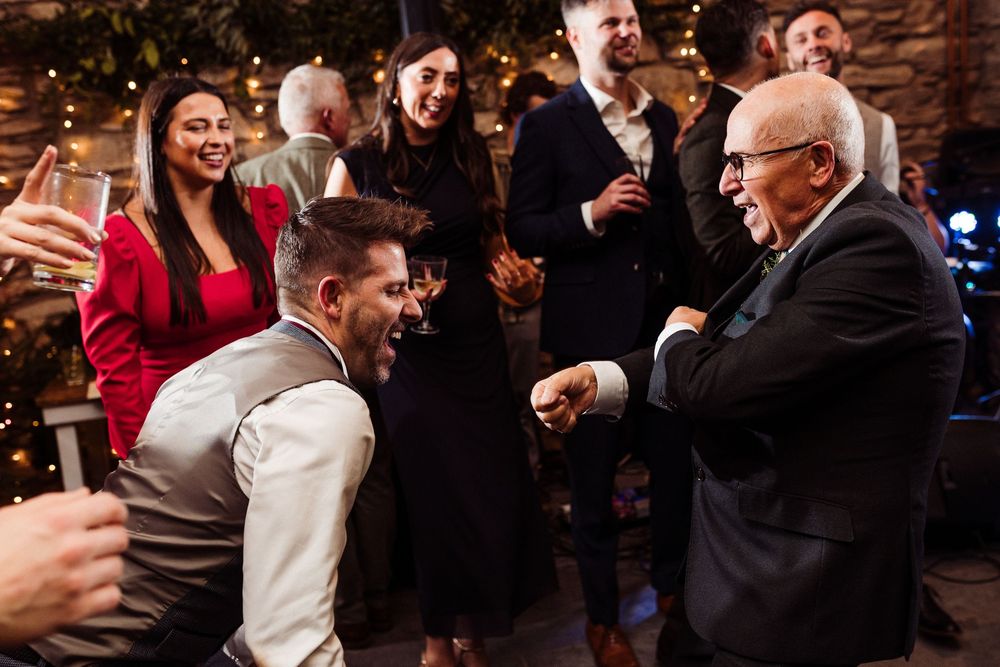 People laugh and embrace during a joyful celebration at an indoor event with warm lighting and festive atmosphere.