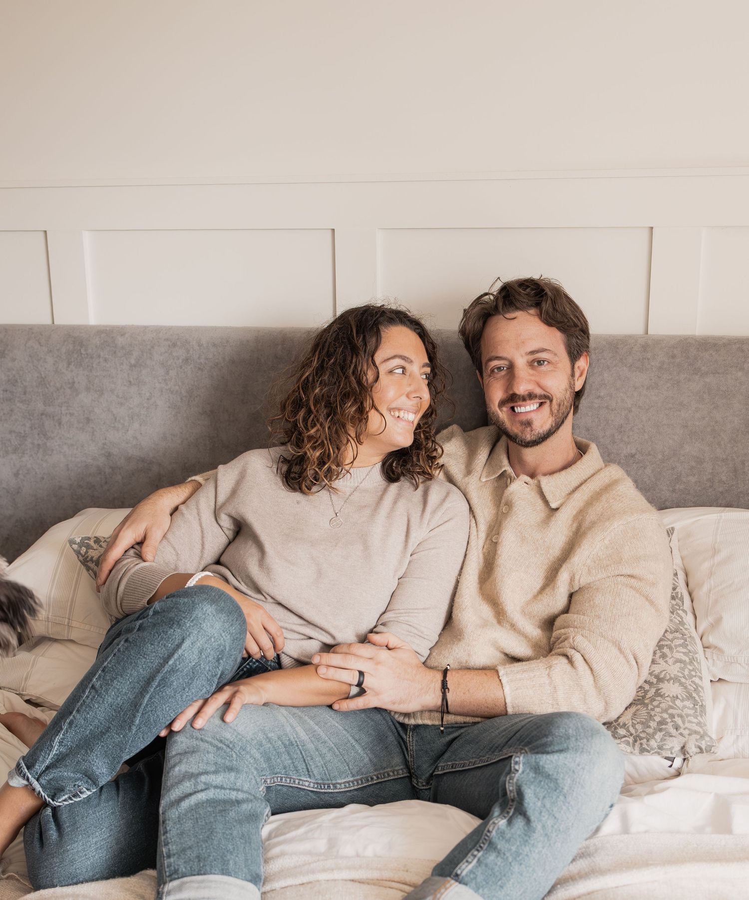 A couple relaxes together on a gray couch, wearing casual outfits of jeans and sweaters in neutral tones. Photography in Buckinghamshire.