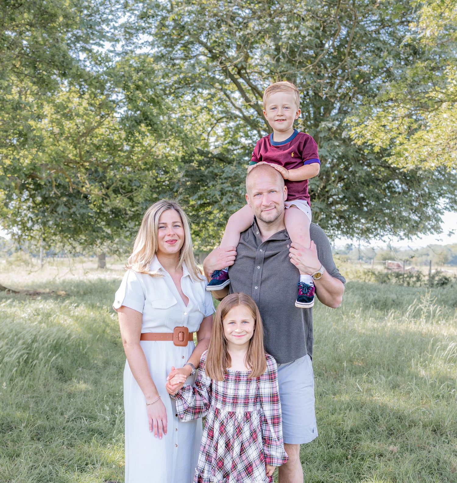 Happy family of four posing outdoors in a green field, parents with two young children on a sunny day.