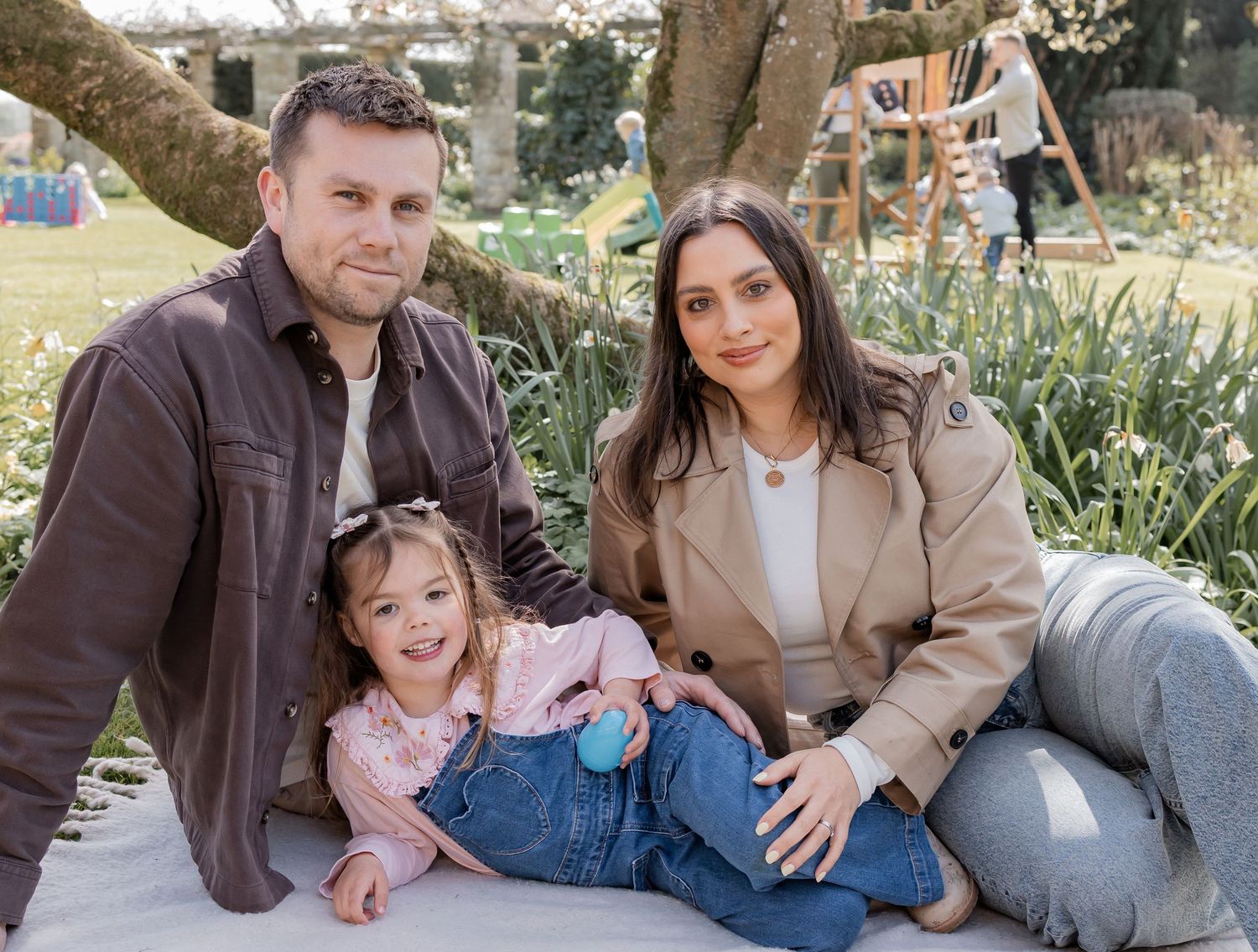 happy family of three poses outdoors on a blanket, smiling in a garden setting. Photography in Buckinghamshire.