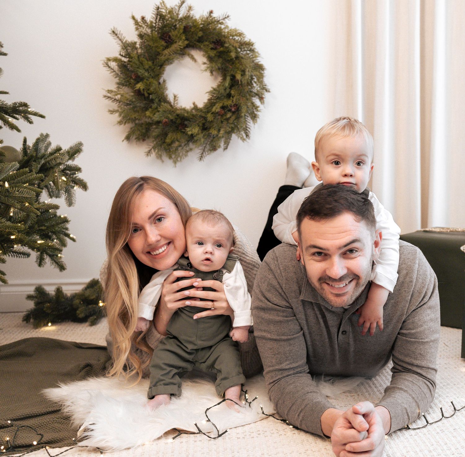 Cozy family portrait on white carpet with evergreen wreath and Christmas decor in background. Photography in Buckinghamshire.