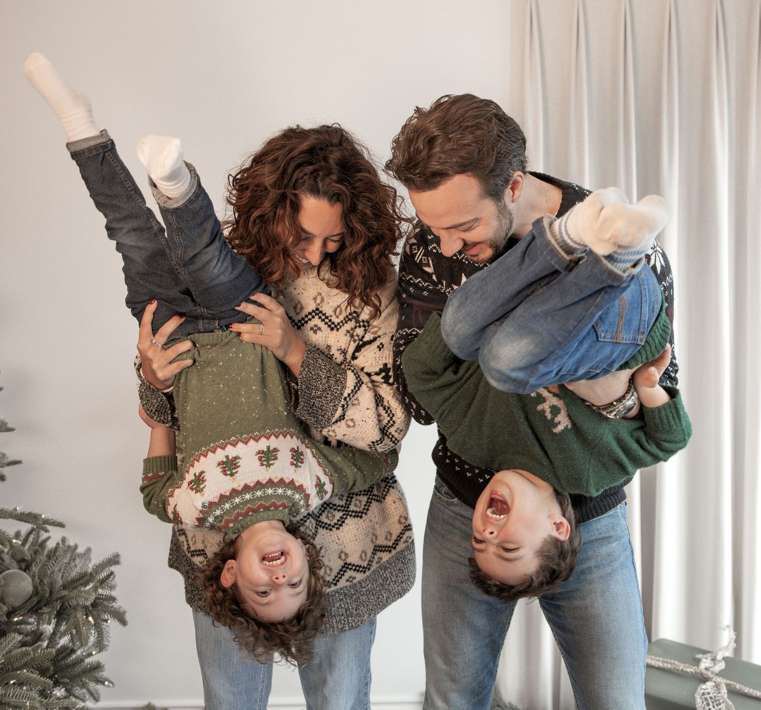 Playful family photoshoot with upside down poses against white wall and Christmas decorations. Photography in Buckinghamshire.