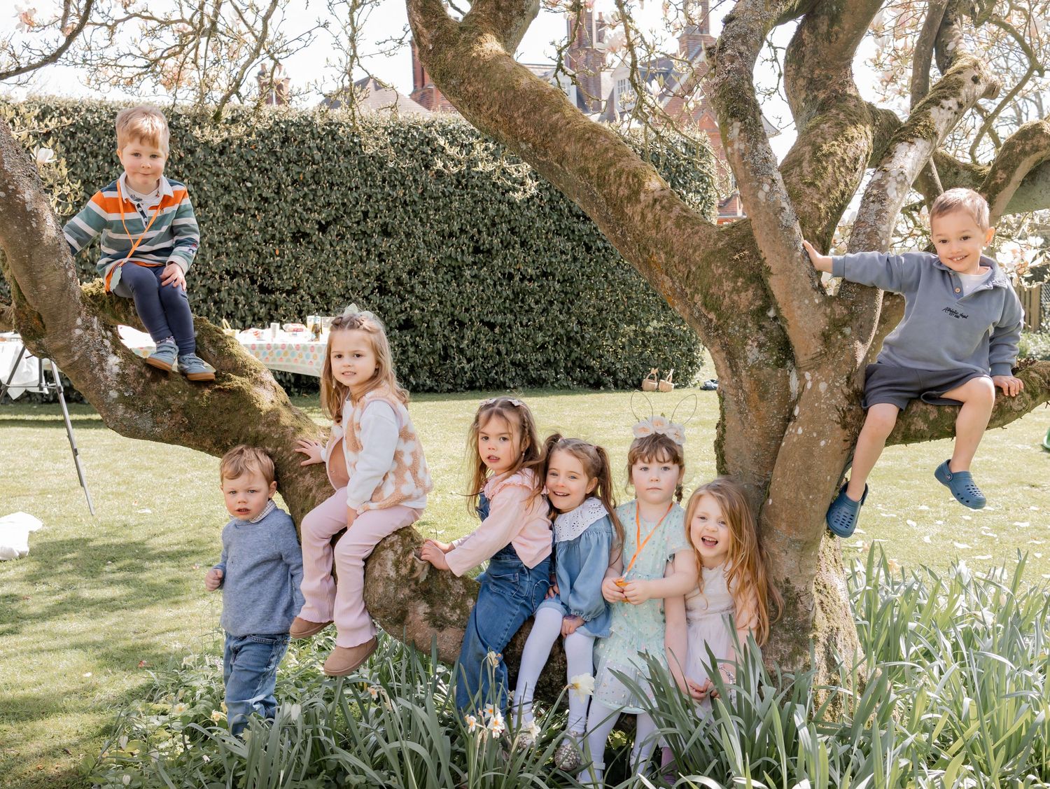 A group of young children posing together around a large tree in a blooming garden on a sunny spring day.photography in Buckinghamshire.