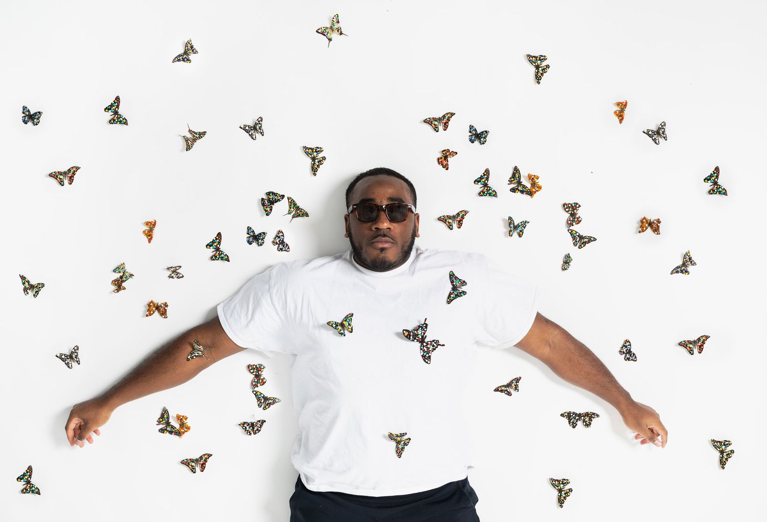 Person in a white t-shirt poses with colorful butterflies flying around against a white background.